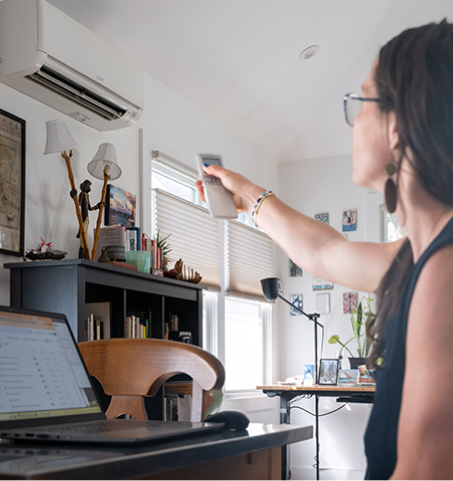 Person uses a remote control to operate a wall-mounted heat pump in a home office.
